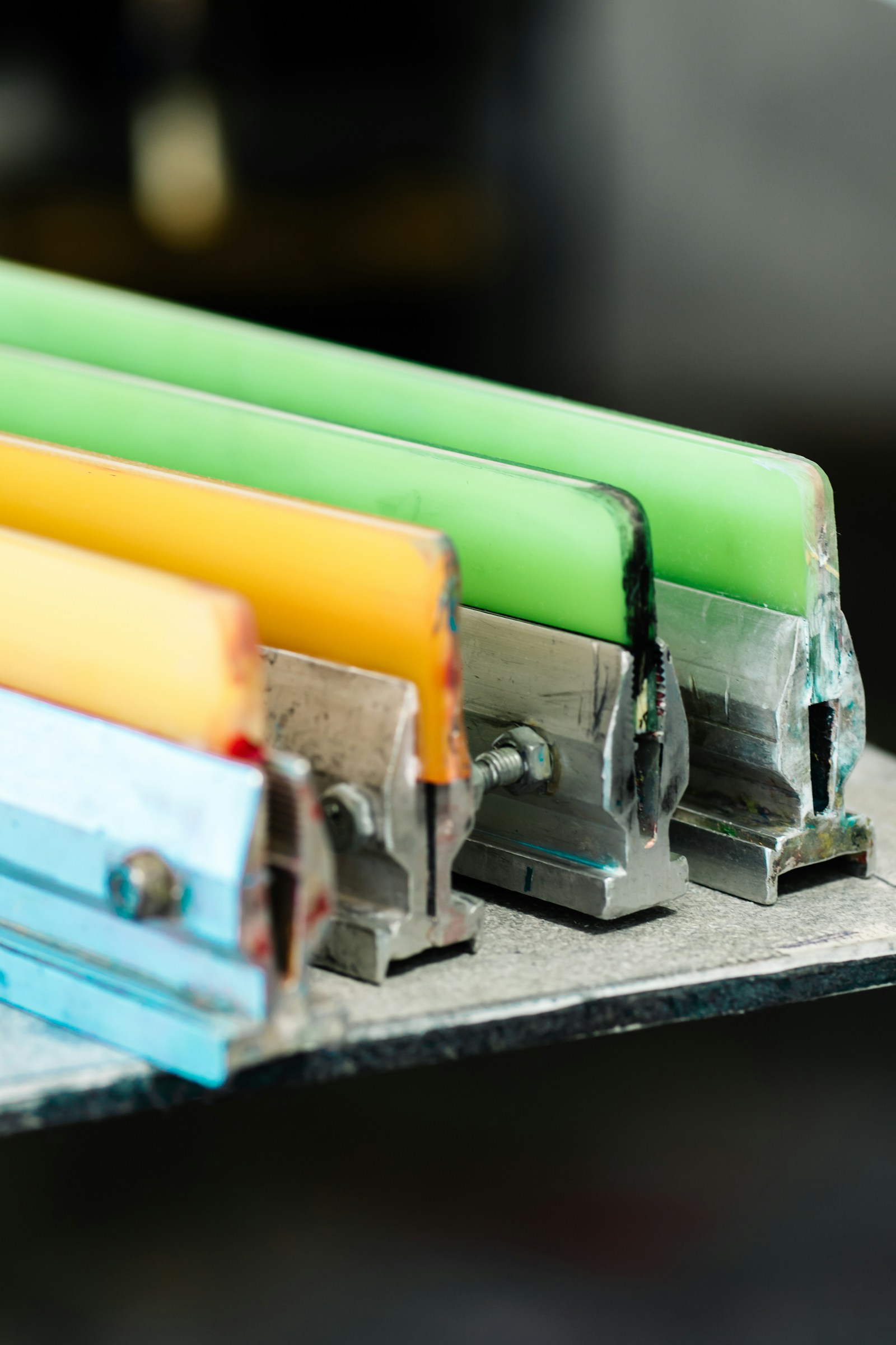 Row of colorful print squeegees resting on a workbench in the Merch Troop studio
