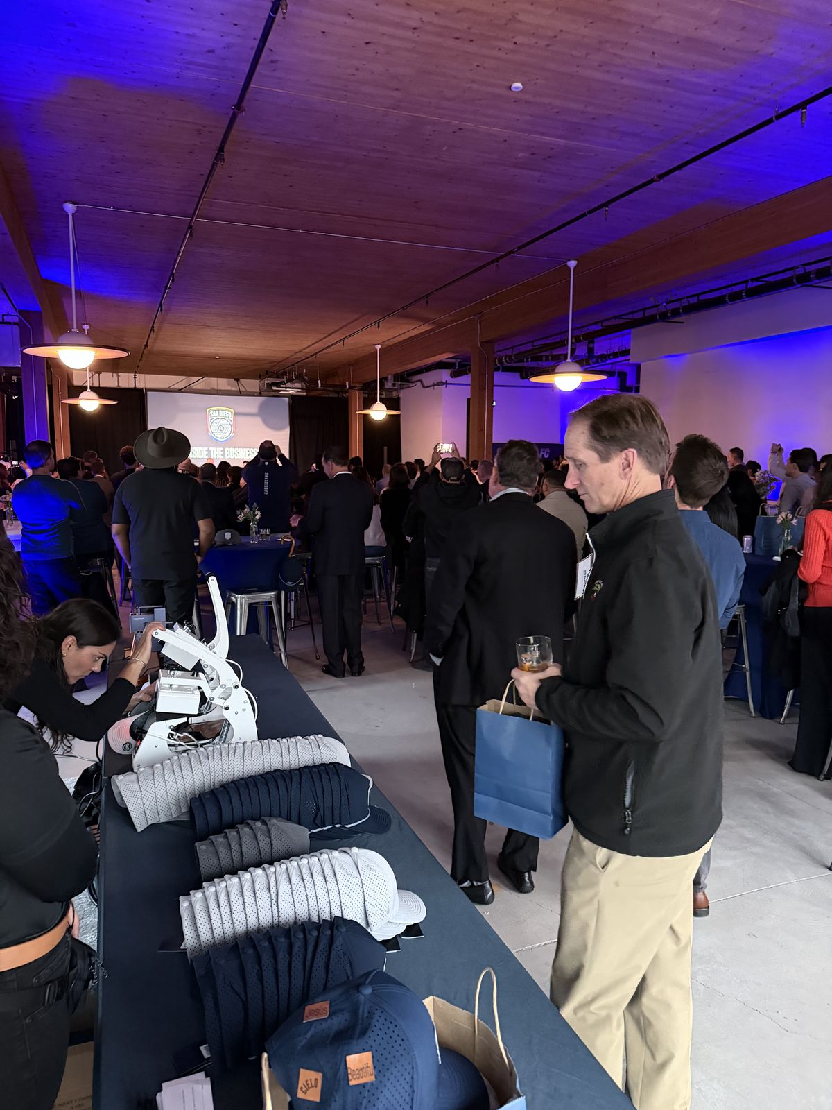 Cap personalization table with heat press at a purple-lit San Diego launch event