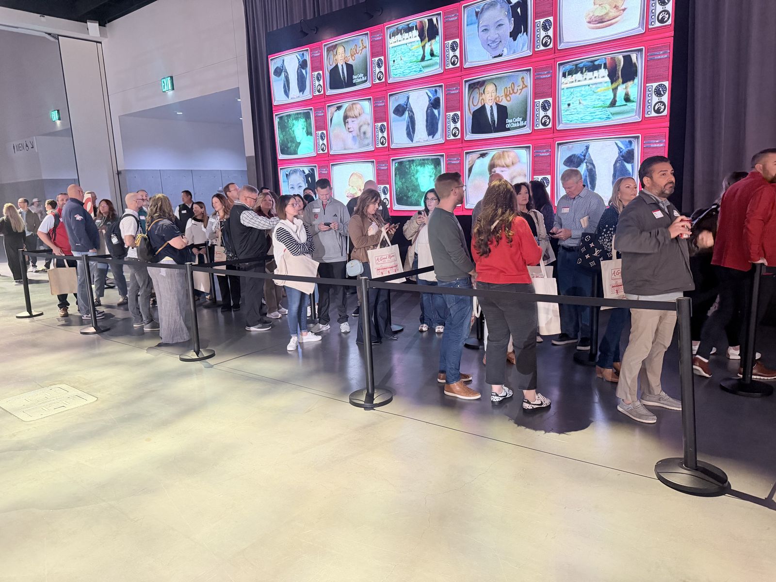 Long stanchioned line of summit guests holding tote bags awaiting personalization
